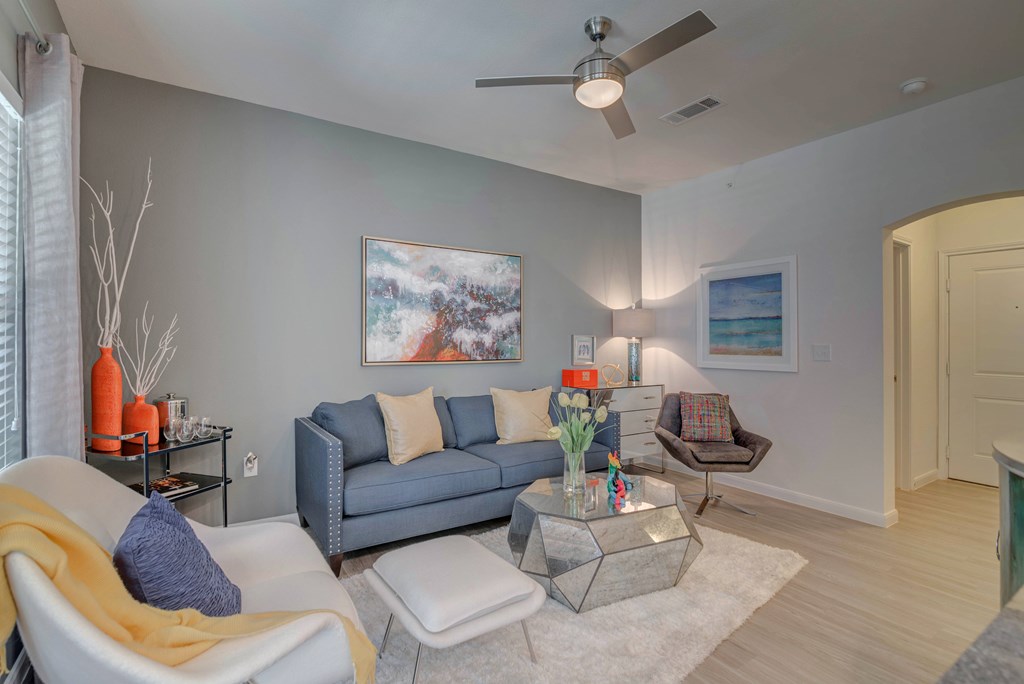 A living room with a grey couch, a white chair, and a painting on the wall.