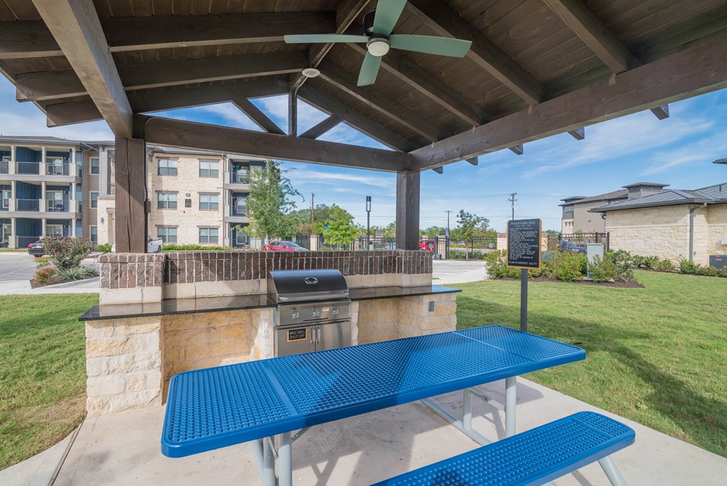 A blue picnic table is under a shelter with a fan.