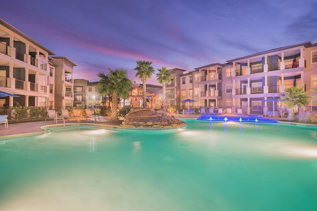 A swimming pool in front of a building with lights on.
