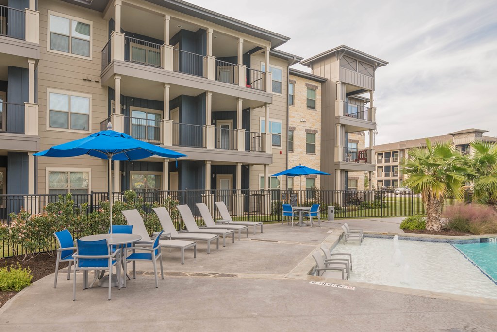 A pool area with lounge chairs and umbrellas in front of apartment buildings.
