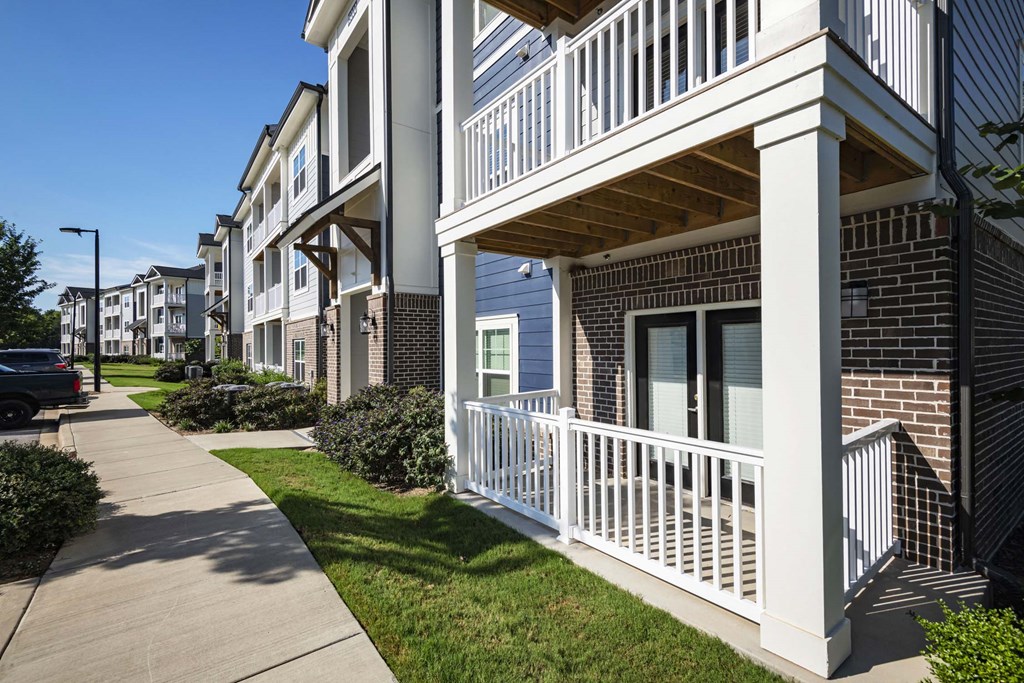 A row of townhouses with white railings and a sidewalk in front at Waterleaf at Neely Ferry Apartments, South Carolina 29680