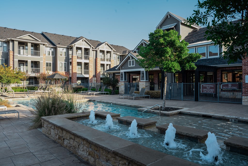 a fountain sits in front of a swimming pool with houses in the background at Platinum Castle Hills, Lewisville