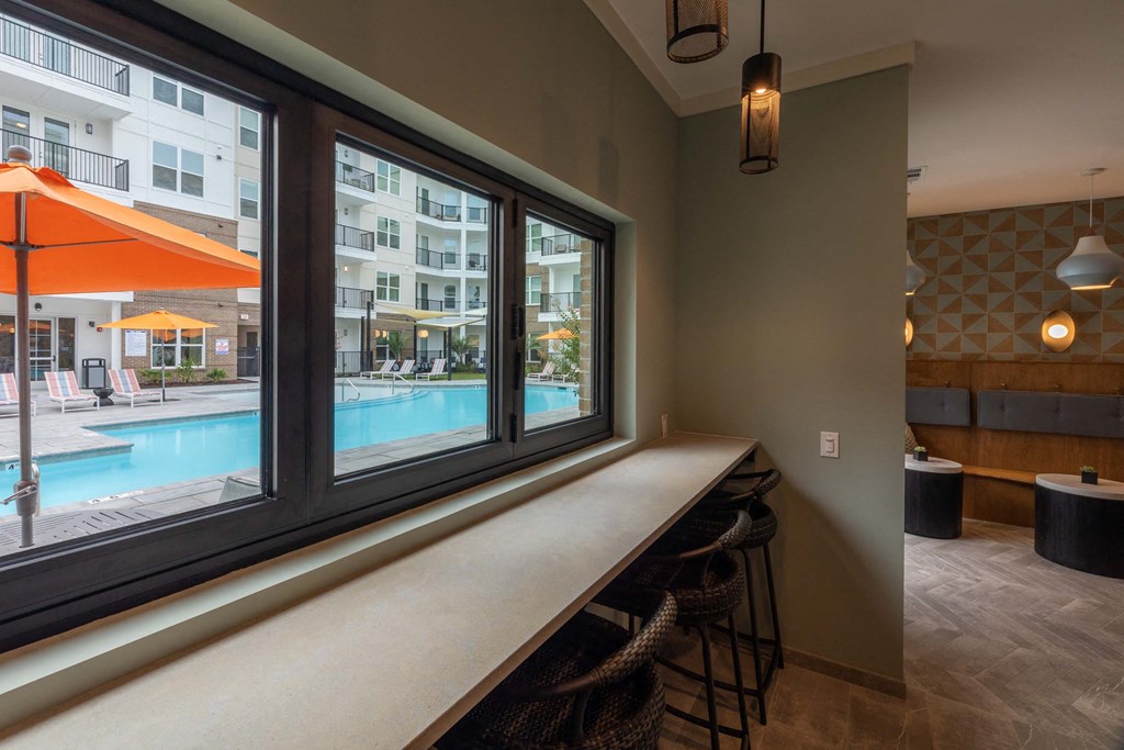 A room with a bar and a view of a pool and apartment building at Hudson at Renaissance Apartments, North Carolina 28405