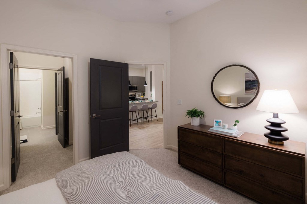 A bedroom with a bed, dresser, mirror, and lamp at Hudson at Renaissance Apartments, North Carolina 28405