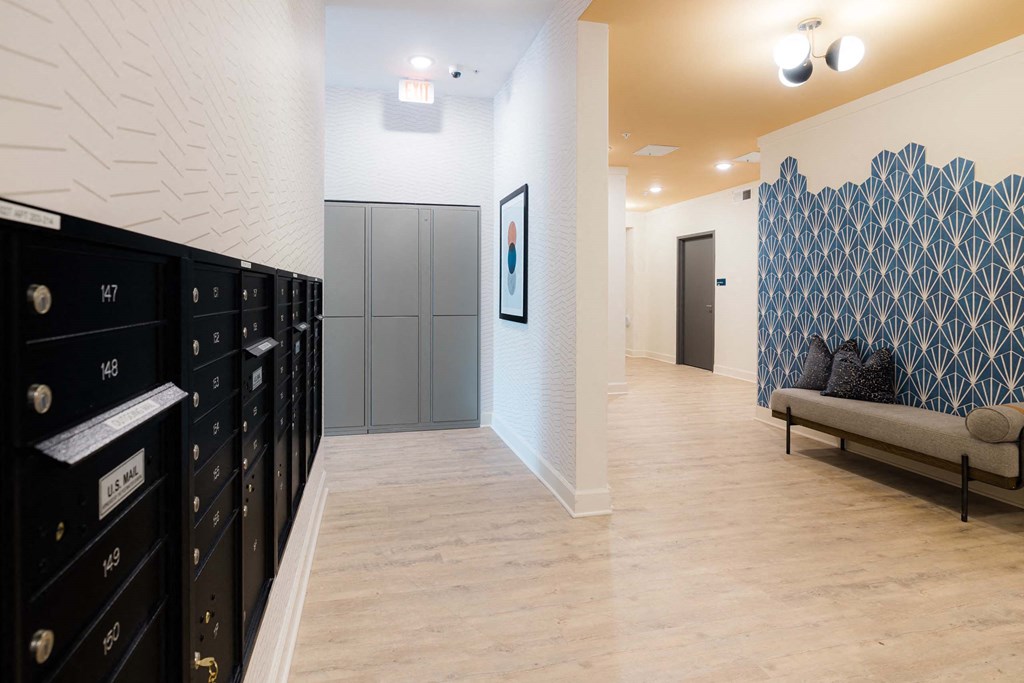A hallway with a row of black lockers on the left and a bench with a blue and white patterned wall behind it on the right at Hudson at Renaissance Apartments, Wilmington