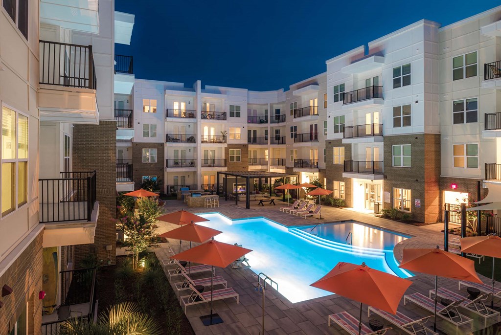 A swimming pool surrounded by orange umbrellas and chairs in a courtyard at night at Hudson at Renaissance Apartments, Wilmington