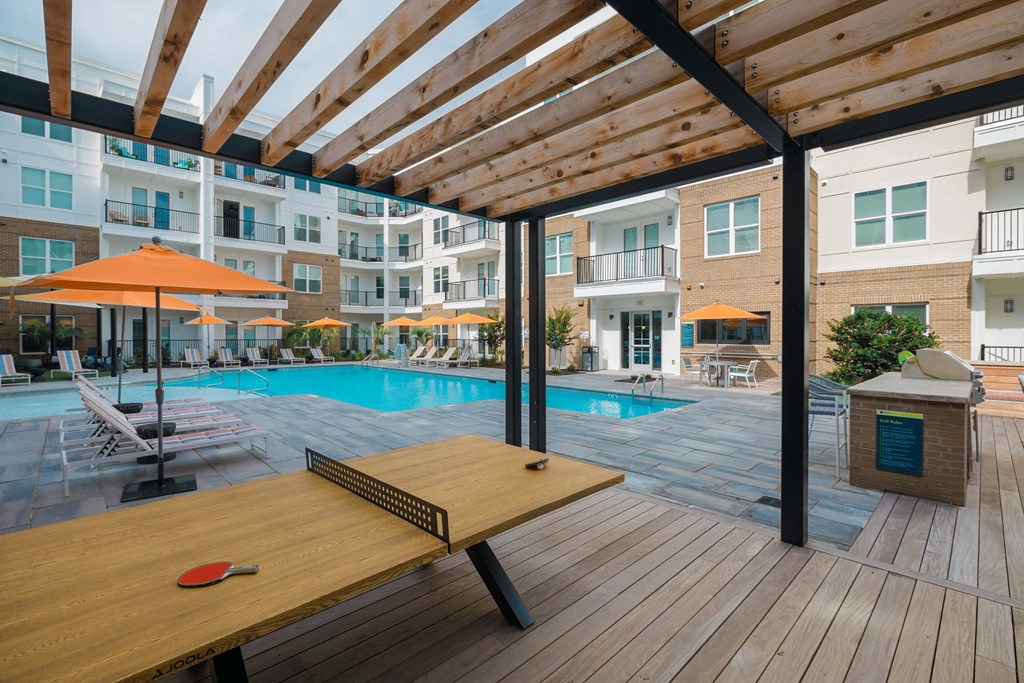 A red paddle is on a wooden table in the foreground of a pool area at Hudson at Renaissance Apartments, Wilmington, North Carolina