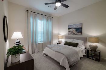 A bedroom with a large bed, a ceiling fan, and a painting on the wall at Hudson at Renaissance Apartments, Wilmington, NC