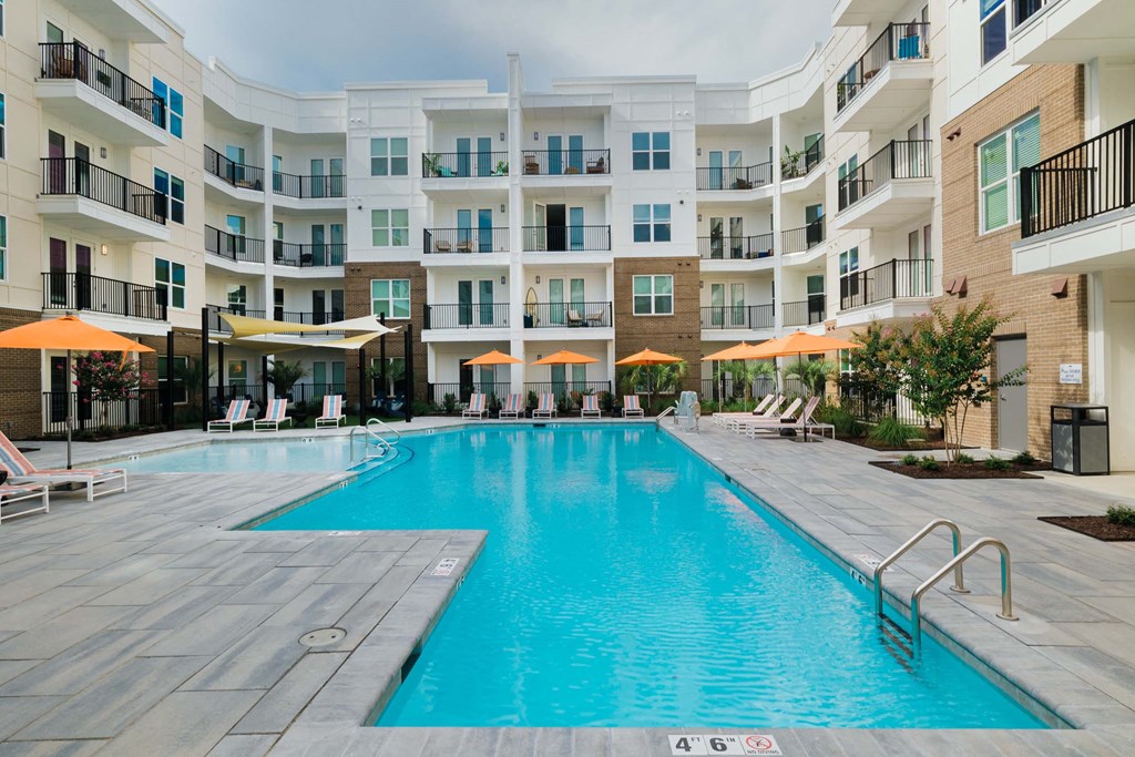 A large swimming pool in a residential building surrounded by lounge chairs and umbrellas at Hudson at Renaissance Apartments, North Carolina