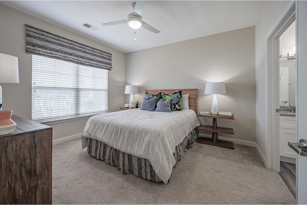 A bedroom with a bed, two lamps, and a window with blinds A bedroom with a bed, two lamps, and a window with blinds at Waterleaf at Neely Ferry Apartments, Simpsonville, 29680