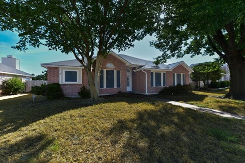 A house with a red brick exterior and a large tree in front.