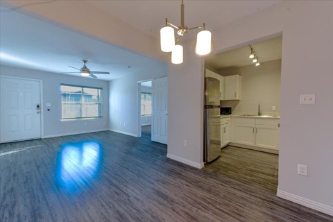 A spacious living room with a ceiling fan and a kitchen in the background.