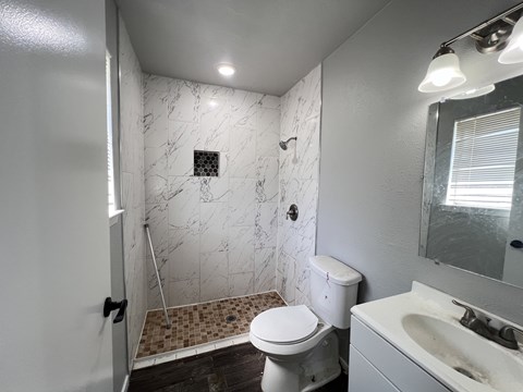A white toilet sits in a bathroom with a marble shower.