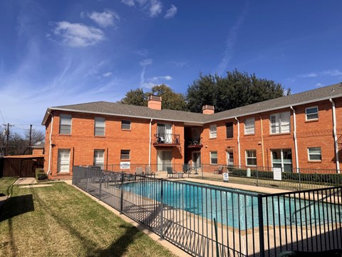 A red brick apartment building with a pool in front.