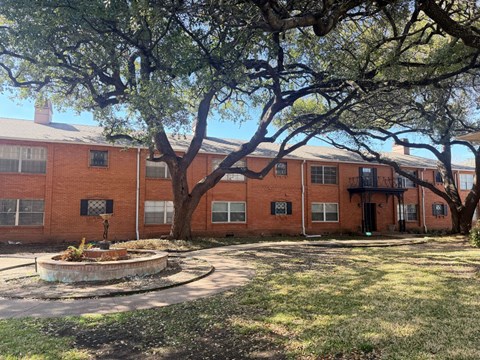 A large tree in front of a red brick building.