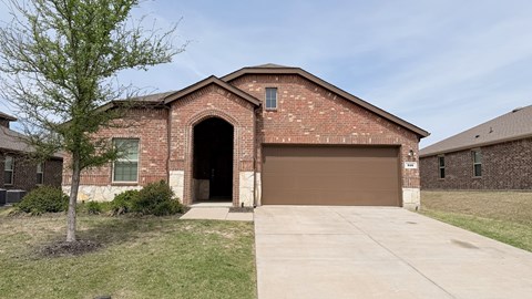 A brick house with a brown garage door and a tree in front.