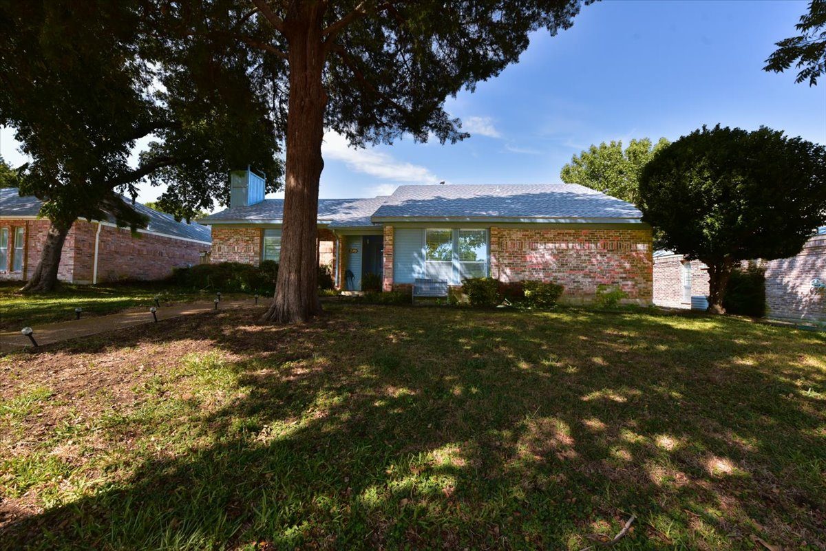 A house with a blue door and windows is surrounded by trees.