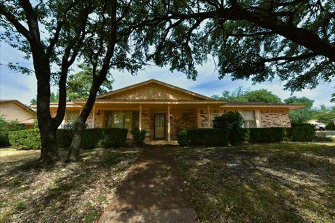 A house with a brown roof and a brown door is surrounded by trees.