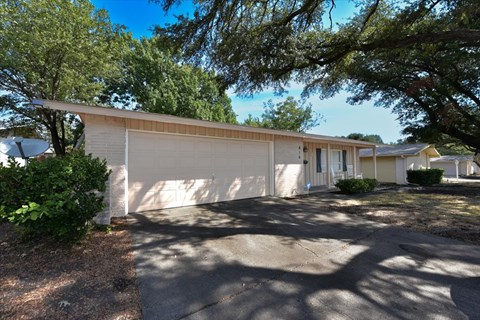 A white building with a garage door is surrounded by trees.