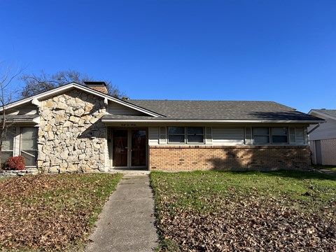 A house with a stone chimney and a grey roof.