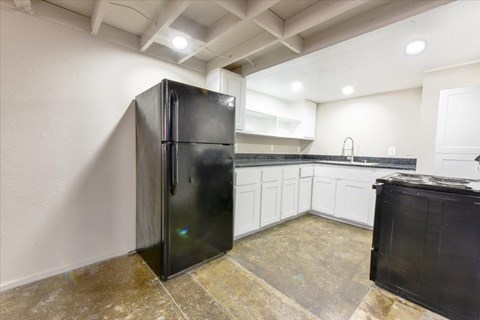 A black refrigerator stands in a kitchen with white walls and a tiled floor.