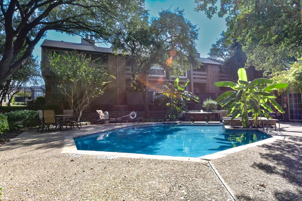 A pool surrounded by trees and a building in the background.