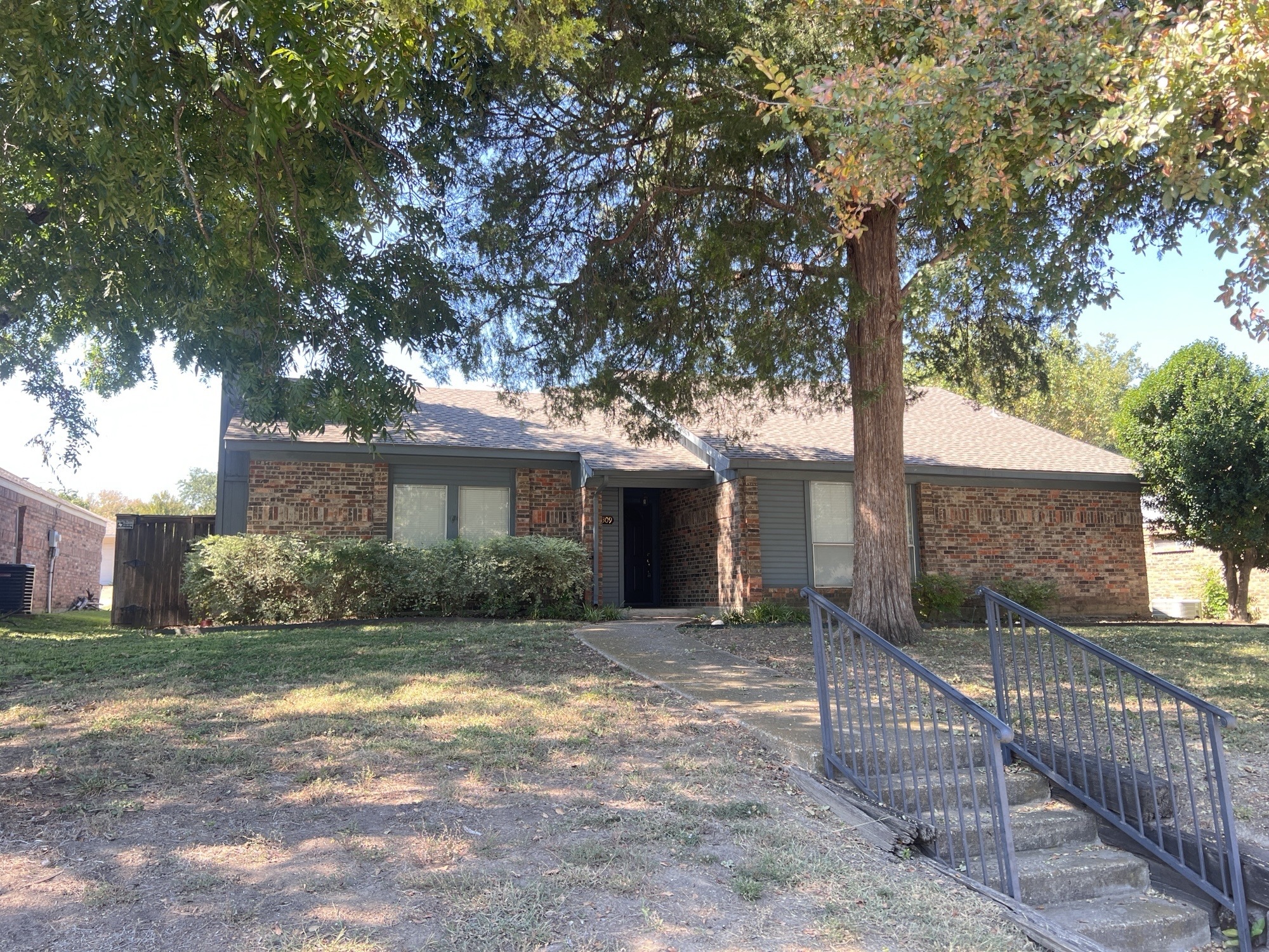 A house with a tree in front and a metal fence.