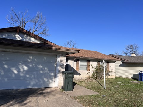 A house with a white garage door and a green trash can.