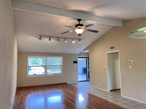 A room with a ceiling fan and a window with a view of a white car and trees.