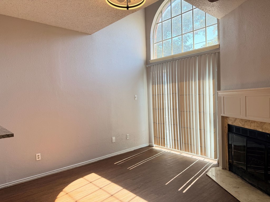 A sunlit room with a fireplace and a large window with vertical blinds.