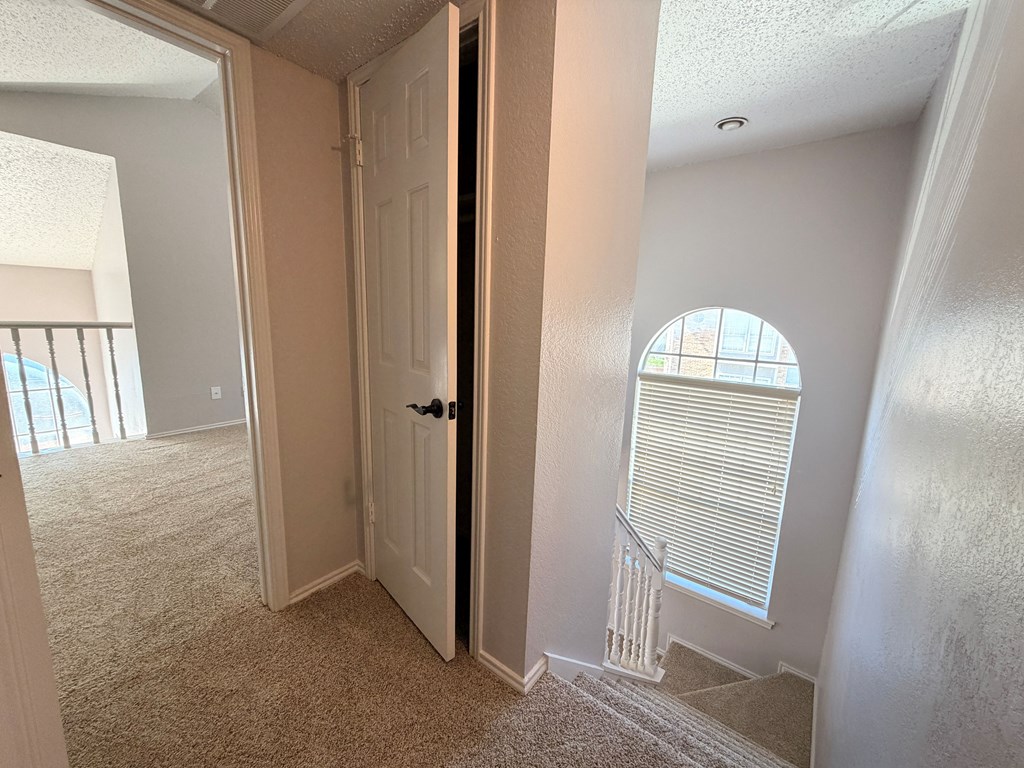A room with a carpeted floor, a staircase, and a window with blinds.