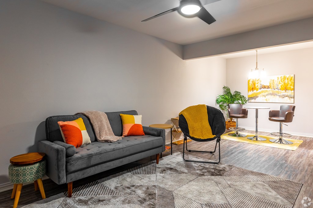 A grey couch with orange and yellow pillows and a black and yellow throw blanket sits in a living room.