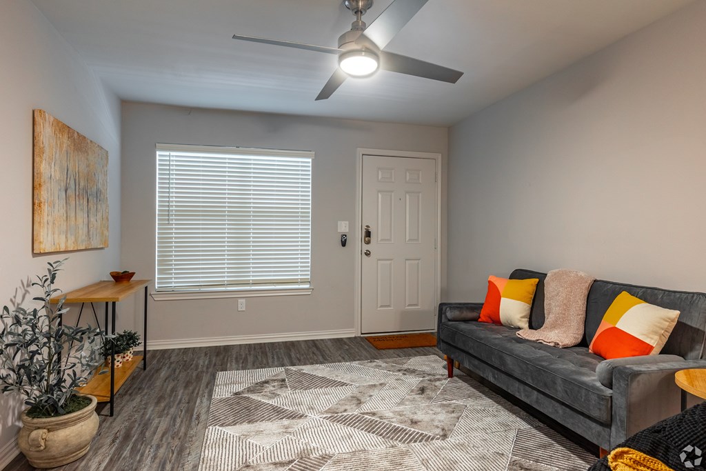 A living room with a grey couch, a rug, a ceiling fan, and a painting on the wall.