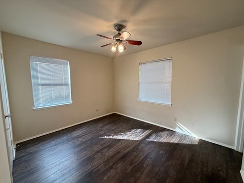 A room with a ceiling fan and two windows.