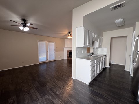 A spacious kitchen with white cabinets and a dark wood floor.