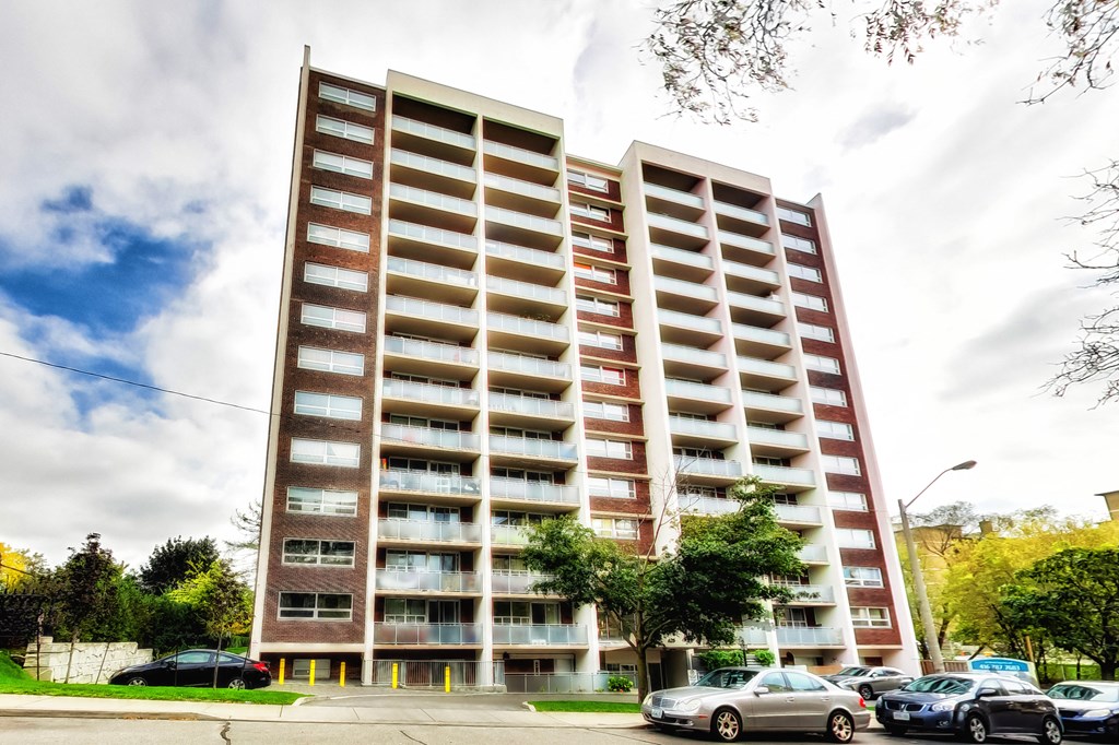 A tall apartment building with a parking lot in front.