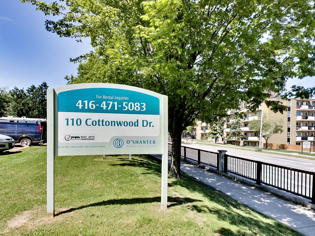 A sign for 110 Cottonwood Dr. is displayed in front of a tree.