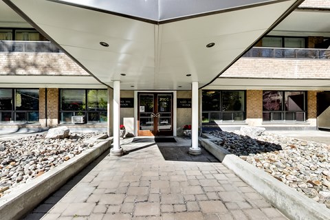 the front entrance of a building with a brick walkway and a rock garden