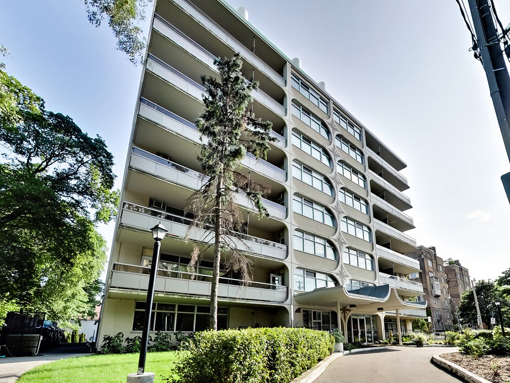 A tall white apartment building with balconies and a green lawn in front.