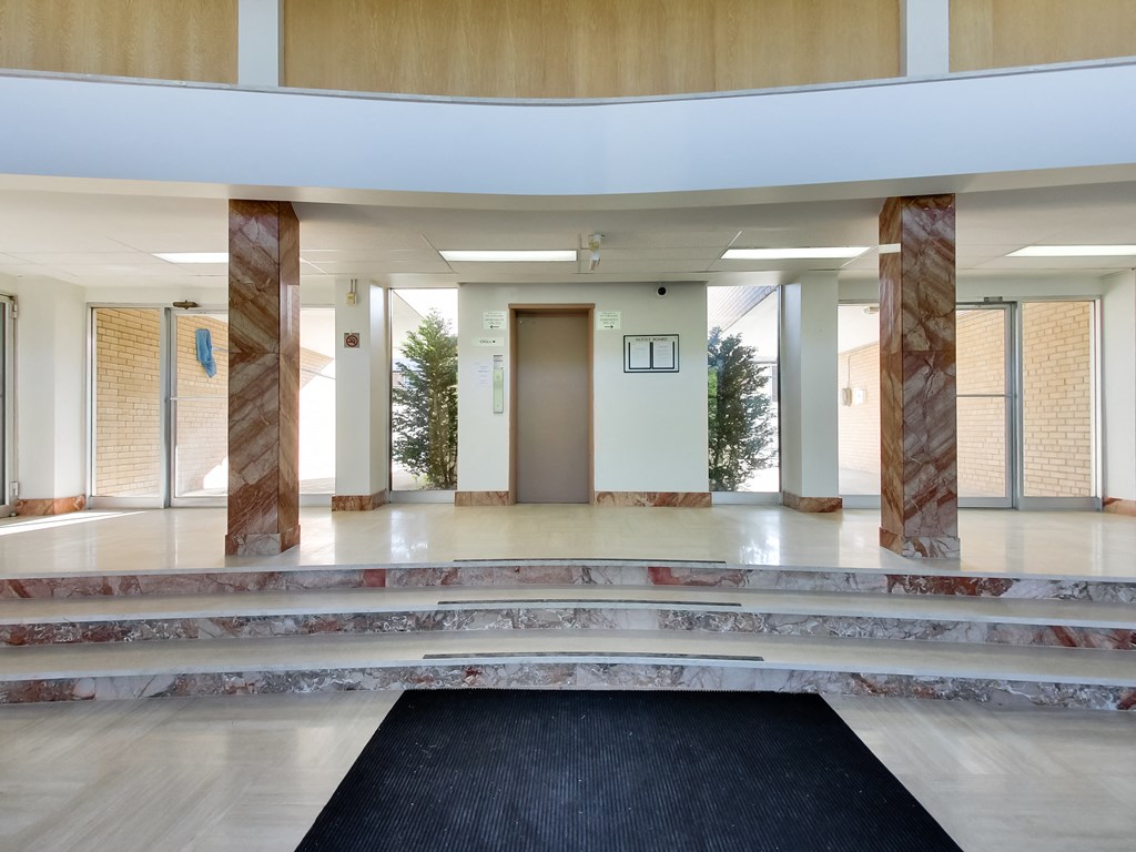 a lobby with pillars and a black rug and a door