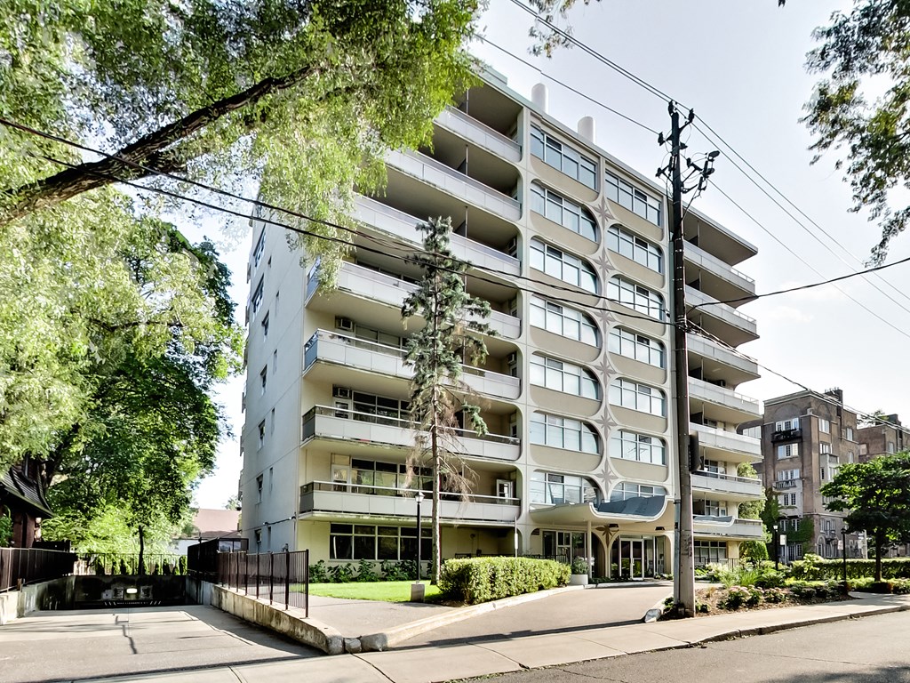 A tall residential building with balconies and a black fence in front.