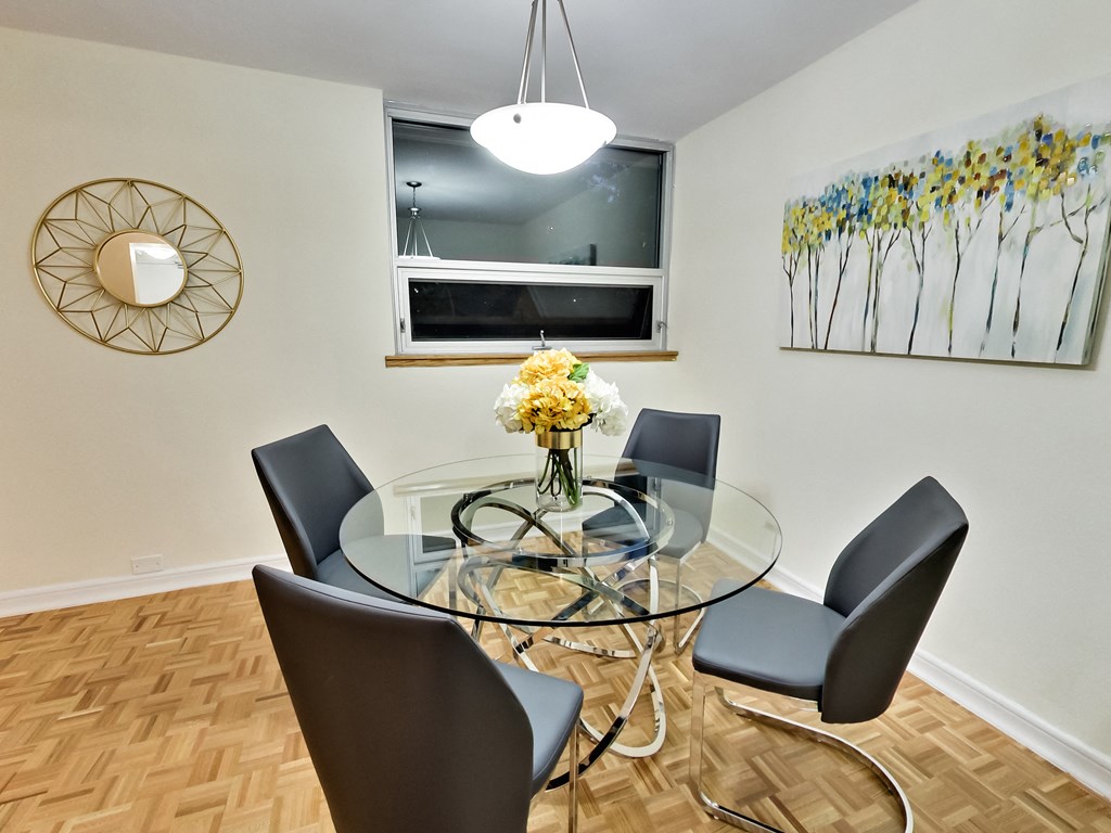 A glass dining table with four chairs and a flower vase on top.