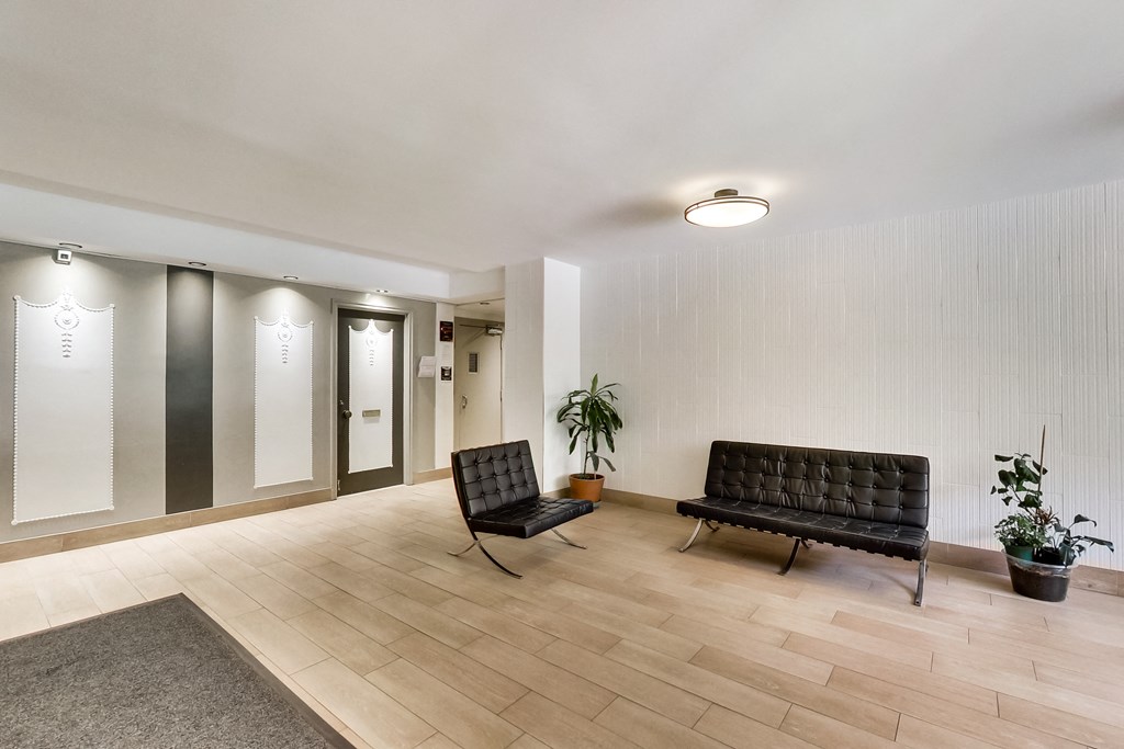 a lobby with two black leather chairs and a potted plant