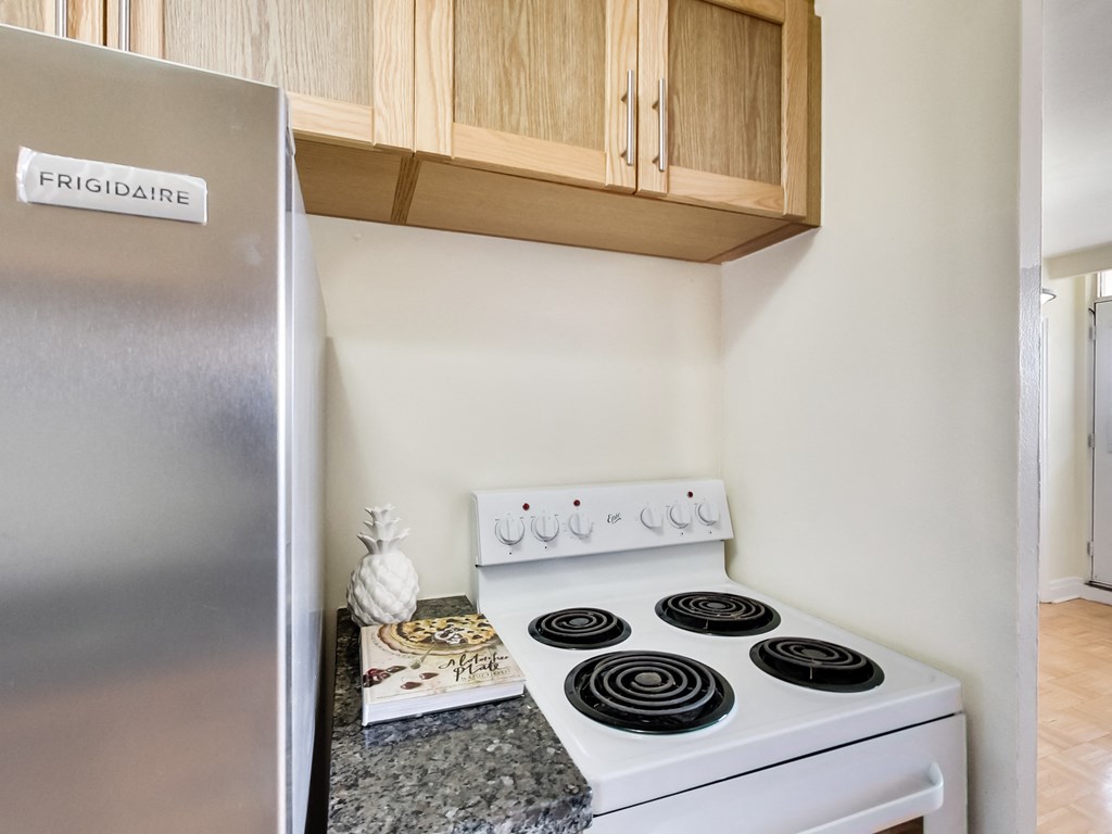 A stainless steel fridge with a white stove in front of wooden cabinets.