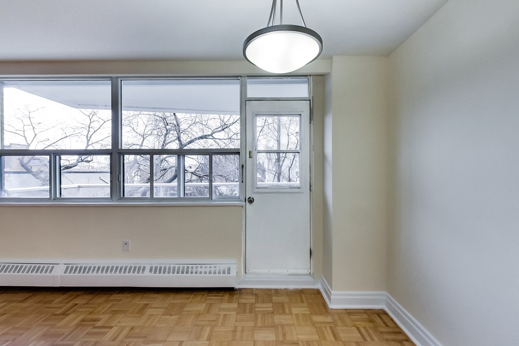 A room with a white door and a window with a view of trees outside.