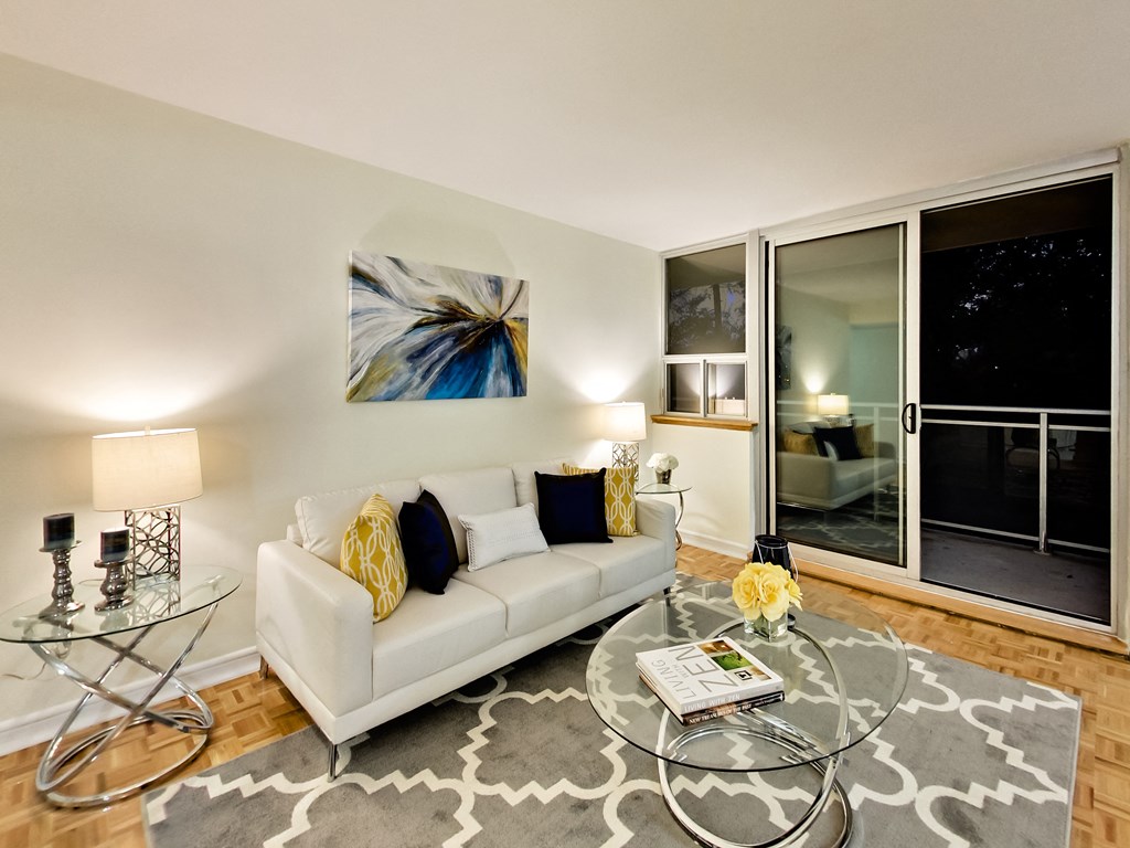 A living room with a white couch, a glass coffee table, and a painting on the wall.