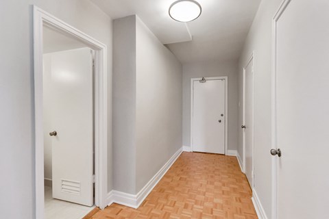 an empty hallway with white walls and wood flooring and a closet