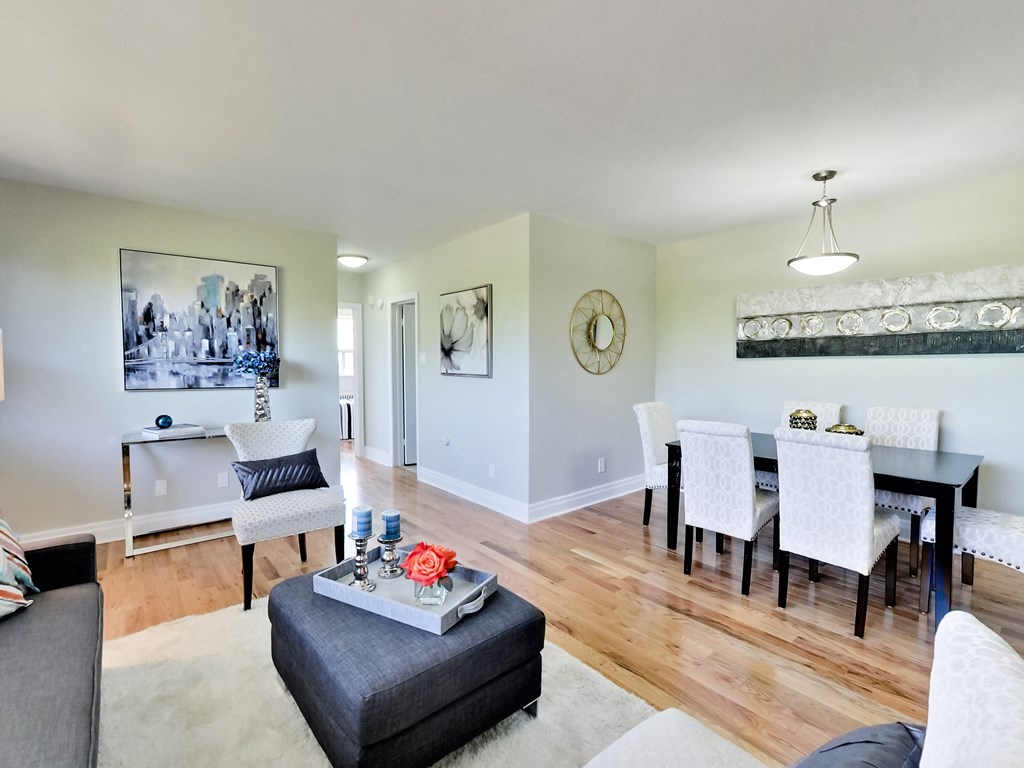 A living room with a grey ottoman and a black table with white chairs.
