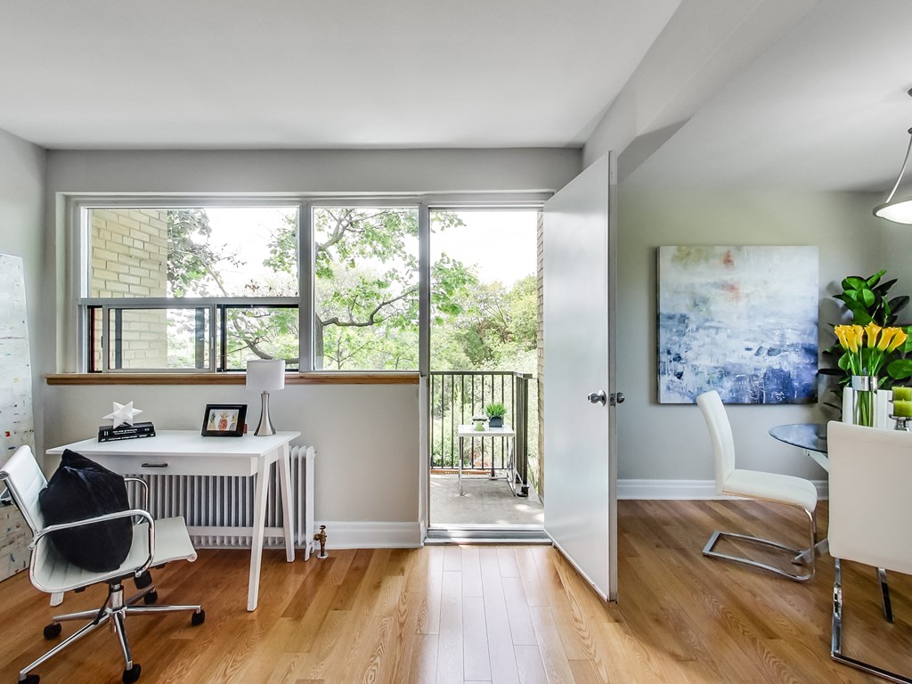 A room with a desk and chairs with a balcony outside.