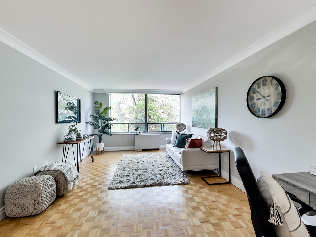A living room with a white couch, a grey rug, and a clock on the wall.